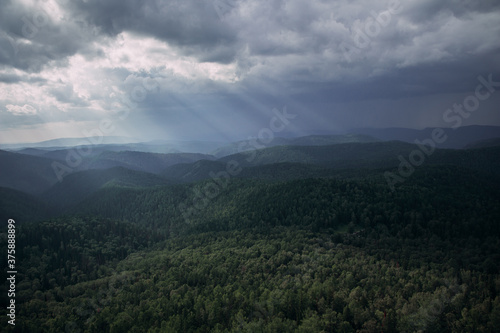 Landscape with haze over evergreen taiga forest hills on rainy day. The rays of the sun break through the clouds. Stolby Nature Reserve in Krasnoyarsk  Russia.