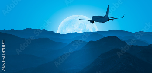 Silhouette of airplane flying over blue mountains with full moon "Elements of this image furnished by NASA" 