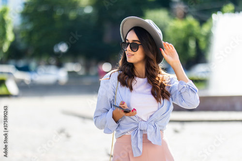 Portrait of young smiling girl tourist standing on city street using smartphone.