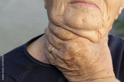 Elderly caucasian woman touching her throat. Sore throat, tonsillitis or thyroid gland problem. 