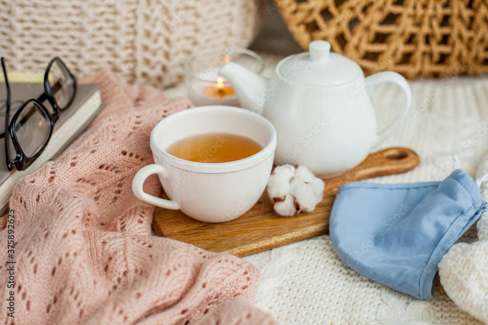 Laptop, face mask, hot tea mug, candle, glasses, kettle, wooden stand. Quarantine. Home Office. Cozy breakfast. Fall.