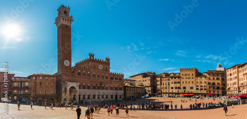 Picturesque panorama of the famous Palazzo Pubblico (town hall) with the bell tower Torre del Mangia, in the historic Piazza del Campo on a sunny day with a blue sky in Siena, Tuscany, Italy. 