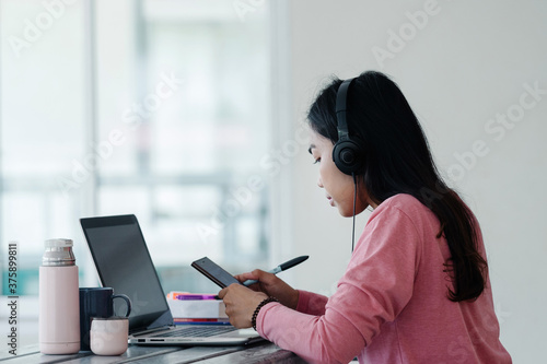 Young Asian freelance businesswoman working on a laptop at home during Coronavirus or COVID-19 pandemic. Young adult learner studying at home concept. Stock photo