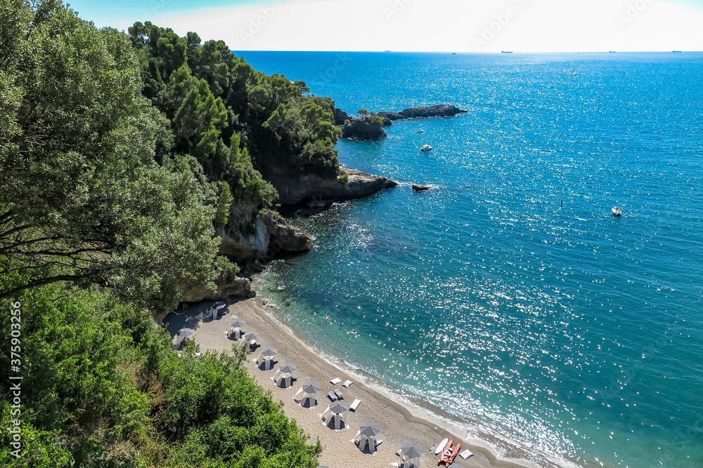 Small white sand beach and blue sea, next to rocky cliff with vegetation, Tellaro village, Gulf of La Spezia, Liguria region, Italy
