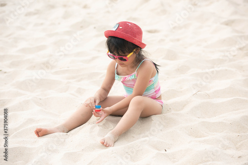 Happy asian child girl playing on white sand at the beach in summer. Asia kid girl with sunglasses and pink hat joyful on sand beach in thailand. people travel holiday concept. 
