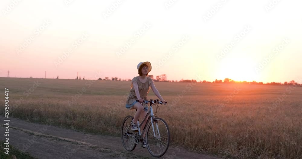 Young woman with hat ride on the bicycle in summer wheat fields Young woman with hat ride on the bicycle in summer wheat fields