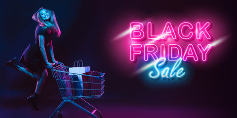 Cheerful, jumping. Portrait of young woman in neon on dark studio backgound. Human emotions, black friday, cyber monday, purchases, sales, finance concept. Copyspace. Seamless post for instagram.
