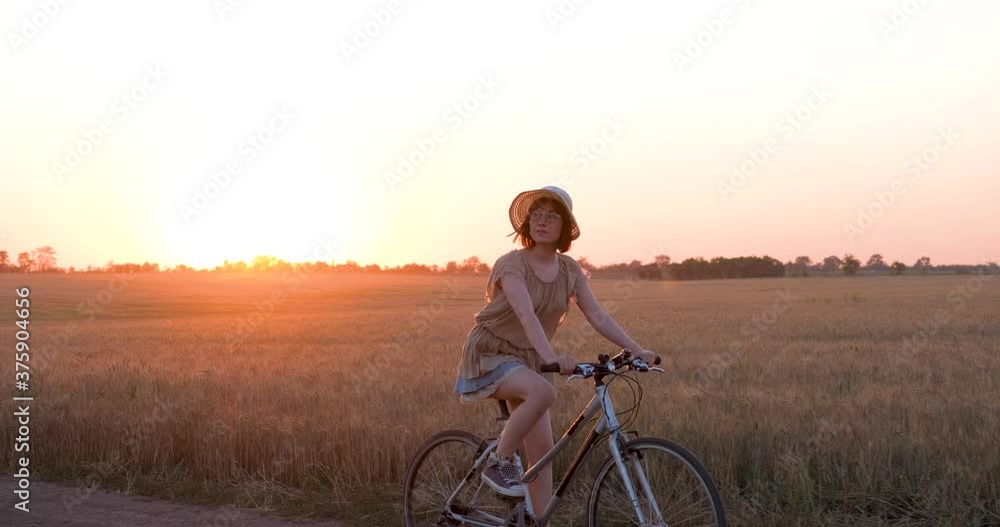 Young woman with hat ride on the bicycle in summer wheat fields Young woman with hat ride on the bicycle in summer wheat fields