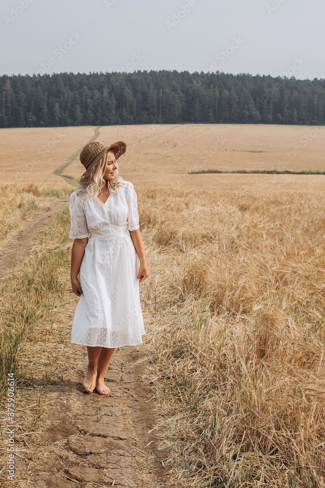A beautiful woman in a white dress and a straw hat walks in the field. A beautiful woman in a white dress and a straw hat walks in the field.