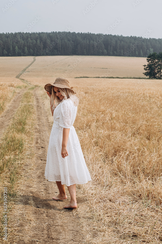 A beautiful woman in a white dress and a straw hat walks in the field. A beautiful woman in a white dress and a straw hat walks in the field.