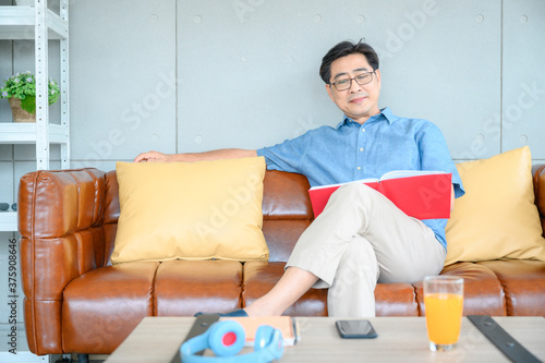 Full length of senior man reading book while relaxing on sofa at home