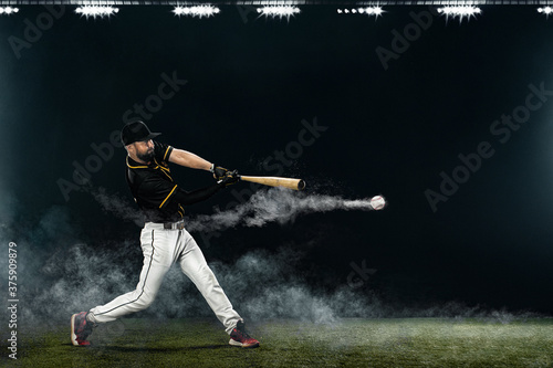 Baseball player with bat taking a swing on grand arena. Ballplayer on dark background in action.