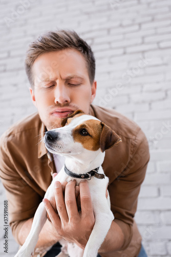 Selective focus of man with face expression embracing jack russell terrier on urban street