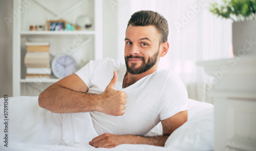 Close up photo of handsome young bearded man lying in bed and relaxing on the morning