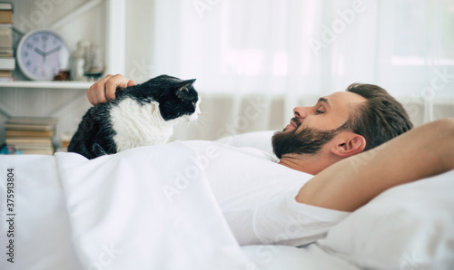 Close up photo of handsome young bearded man lying in bed and relaxing on the morning
