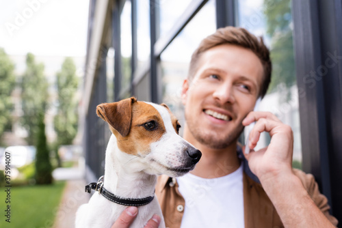 selective focus of young man talking on smartphone while holding jack russell terrier dog on city street