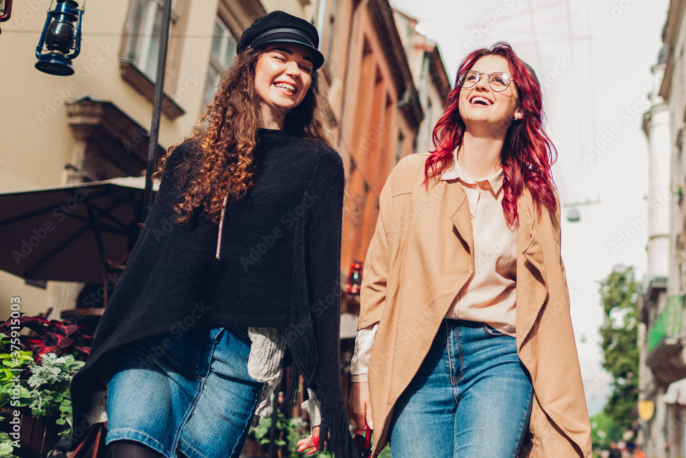 Two young women walking on city street laughing. Friends talking and having fun together Two young women walking on city street laughing. Friends talking and having fun together