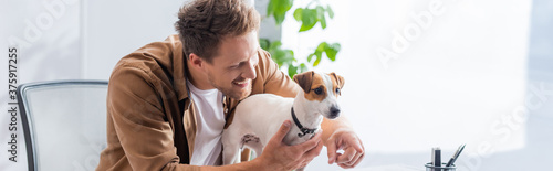 panoramic shot of young businessman pointing with finger near jack russell terrier dog in office