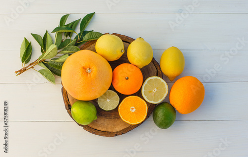 Citrus fruits with leaves on cutting board and wooden background, top view.