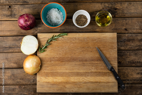 View of a wooden cutting board and knife with onion and seasonings arranged on a on a textured woode