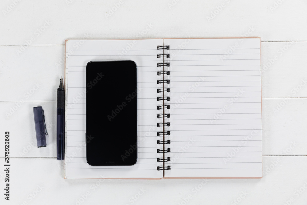 Fototapeta premium View of a black smartphone, a notebook and a black pen on plain white background