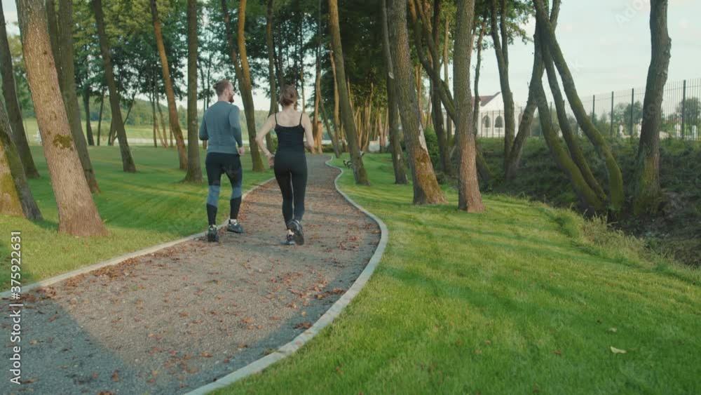 Shot back man and woman running in park together jogging at outdoor workout at sunlight sportswear active young workout sport runner fitness cardio summer slow motion Shot back man and woman running in park together jogging at outdoor workout at sunlight sportswear active young workout sport runner fitness cardio summer slow motion
