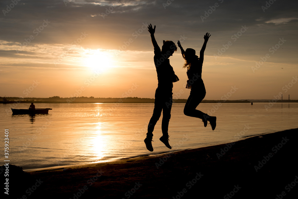 silhouette of a woman and a man jumping on the beach, sunset, gold, orange