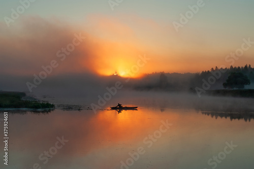Silhouette image of a fisherman on a wooden boat. Sunrise over the river and fog