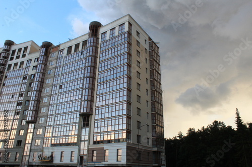 the building is a modern residential building complex with a glass facade during construction on the background of a blue sky with clouds illuminated by the sun at sunset