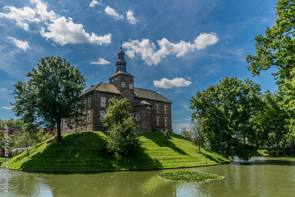 Limbricht castle surrounded by water and green trees, wonderful sunny day with a blue sky and white clouds in south Limburg in the Netherlands Holland