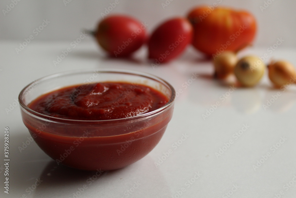 red tomato sauce ketchup in a glass salad bowl saucepan on a white background are vegetables in the background red tomatoes red tomato sauce ketchup in a glass salad bowl saucepan on a white background are vegetables in the background red tomatoes