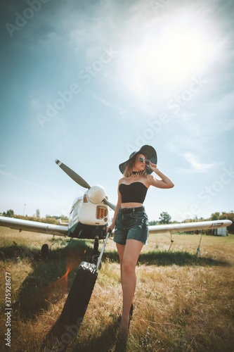 woman in hat and sunglasses standing near airplane with propeller outdoors