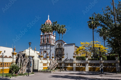 Outside the church of San Pedro Apóstol with its white walls and yellow and red details, wonderful and sunny day in Tlaquepaque Jalisco Mexico photo
