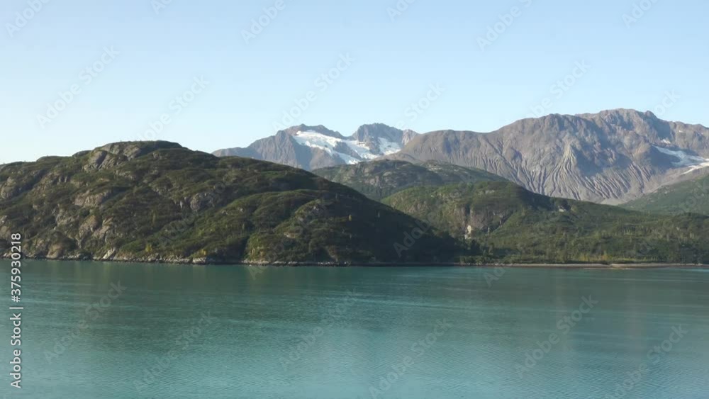 Glacier Bay, Alaska /US - October 30th 2019: A view from the cruising ship on a beautiful mountains with snow, blue sky and green water of natural preserve Glacier Bay, Alaska /US - October 30th 2019: A view from the cruising ship on a beautiful mountains with snow, blue sky and green water of natural preserve