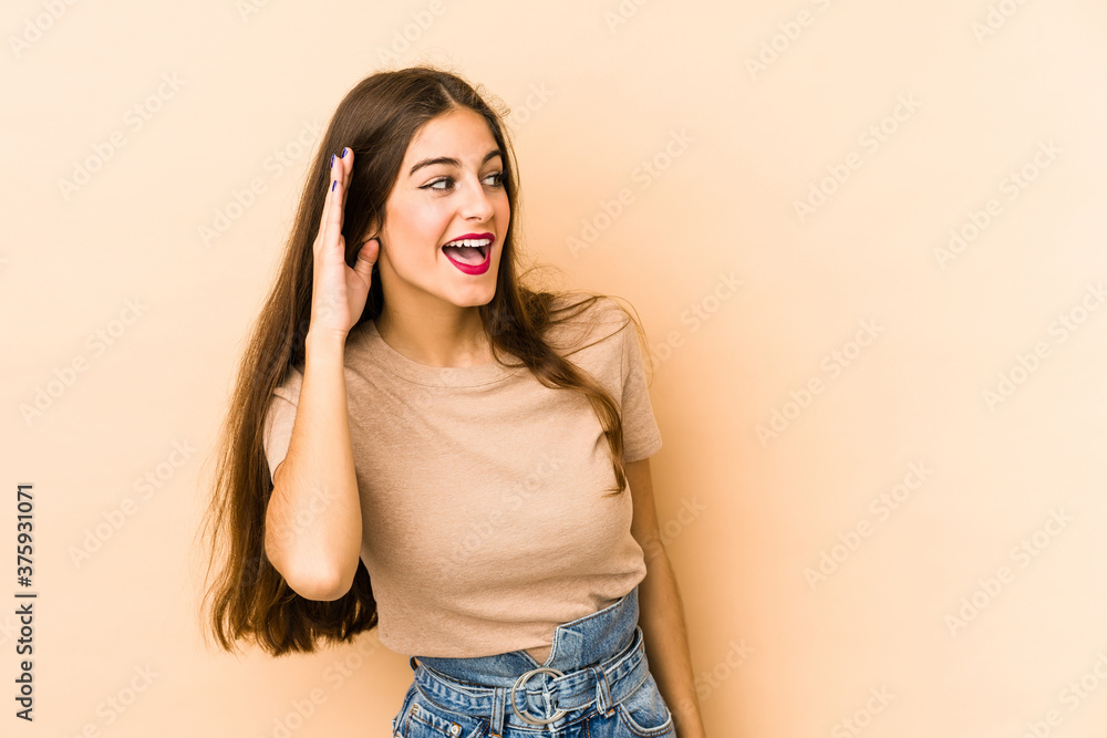Young caucasian woman isolated en beige background trying to listening a gossip. Young caucasian woman isolated en beige background trying to listening a gossip.