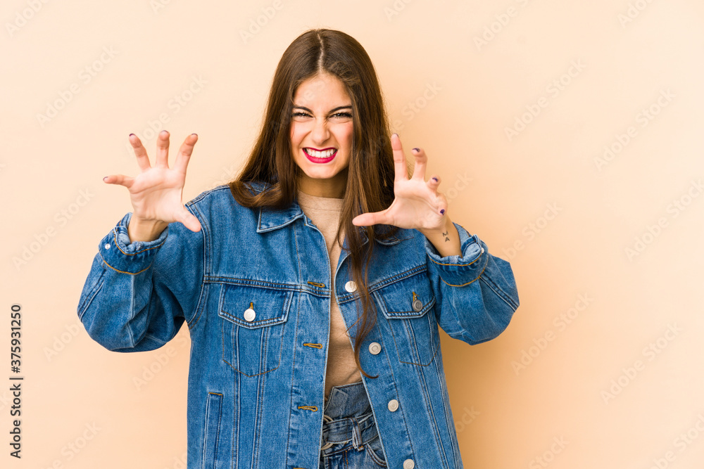 Young caucasian woman isolated en beige background showing claws imitating a cat, aggressive gesture. Young caucasian woman isolated en beige background showing claws imitating a cat, aggressive gesture.