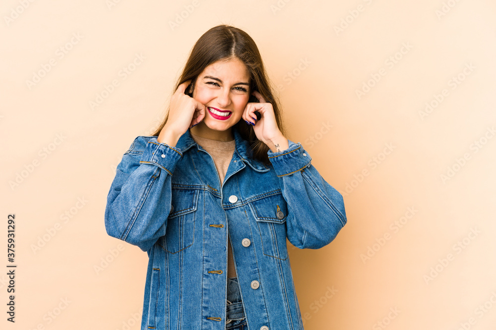 Young caucasian woman isolated en beige background covering ears with fingers, stressed and desperate by a loudly ambient. Young caucasian woman isolated en beige background covering ears with fingers, stressed and desperate by a loudly ambient.