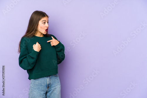 Young caucasian woman isolated on purple background surprised pointing with finger, smiling broadly.