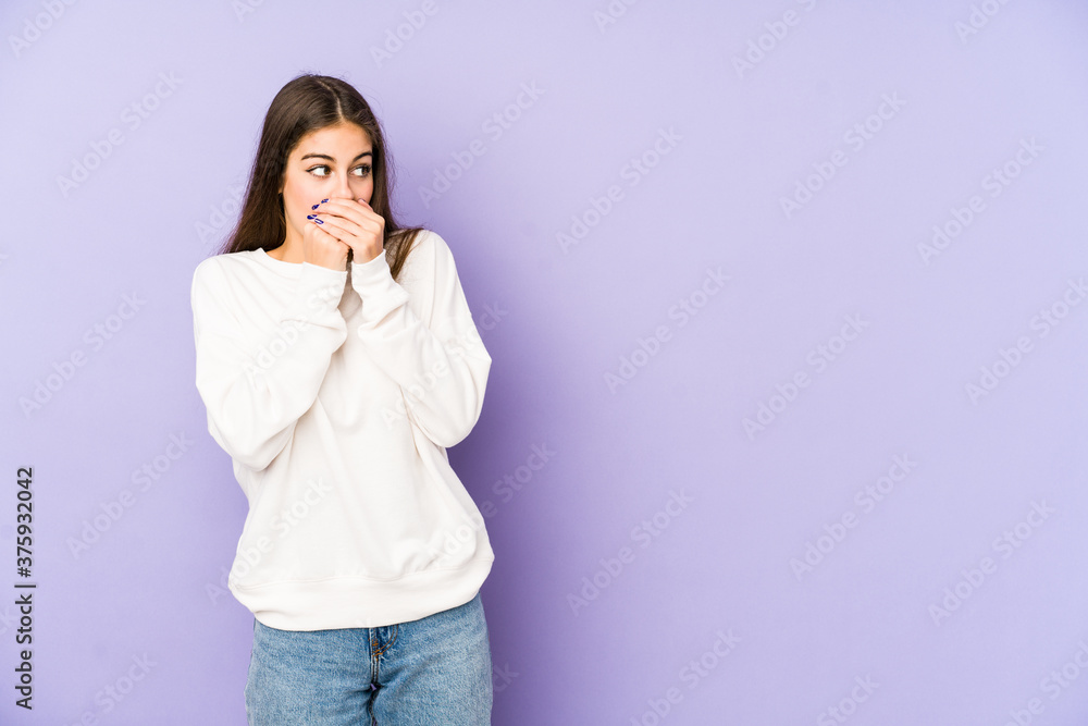 Young caucasian woman isolated on purple background thoughtful looking to a copy space covering mouth with hand. Young caucasian woman isolated on purple background thoughtful looking to a copy space covering mouth with hand.