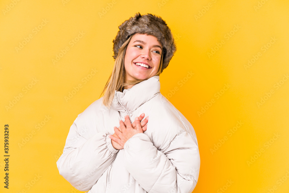 Young blonde caucasian woman wearing a winter clothes isolated has friendly expression, pressing palm to chest. Love concept. Young blonde caucasian woman wearing a winter clothes isolated has friendly expression, pressing palm to chest. Love concept.