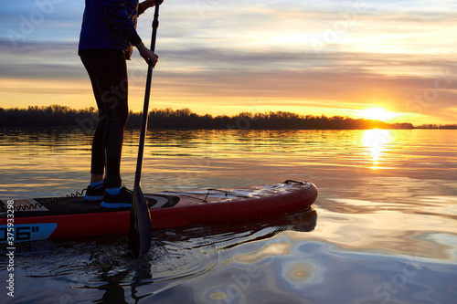 Legs of a girl on stand up paddle board (SUP) with a paddle at winter river at sunset photo