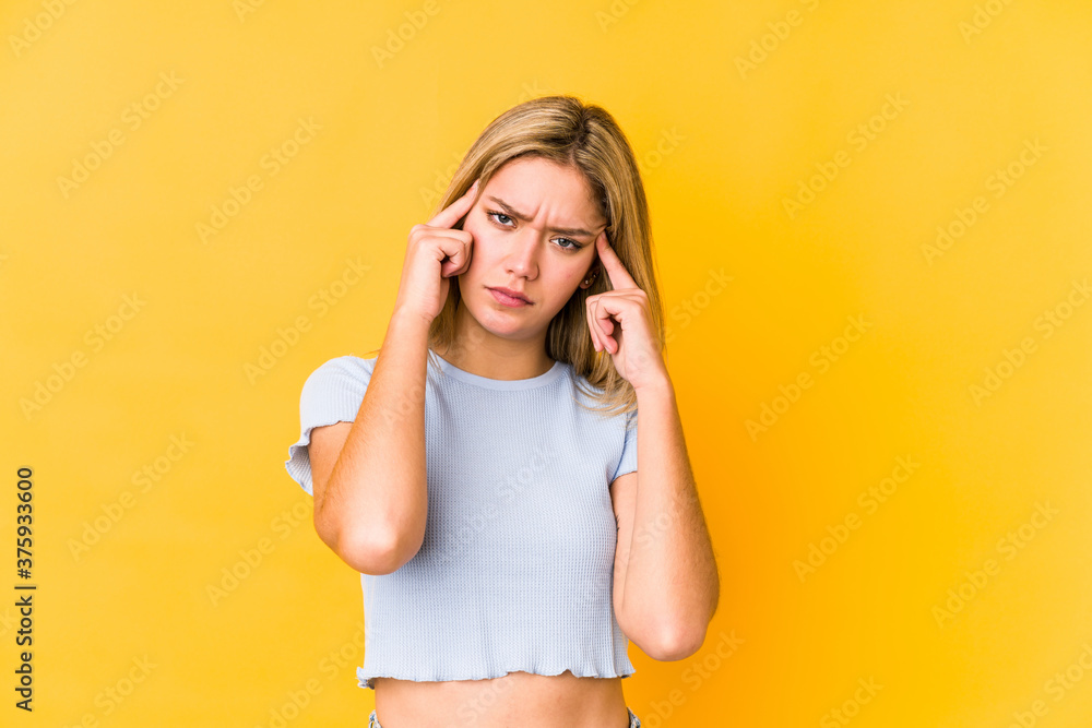 Young blonde caucasian woman isolated on a yellow background focused on a task, keeping forefingers pointing head. Young blonde caucasian woman isolated on a yellow background focused on a task, keeping forefingers pointing head.