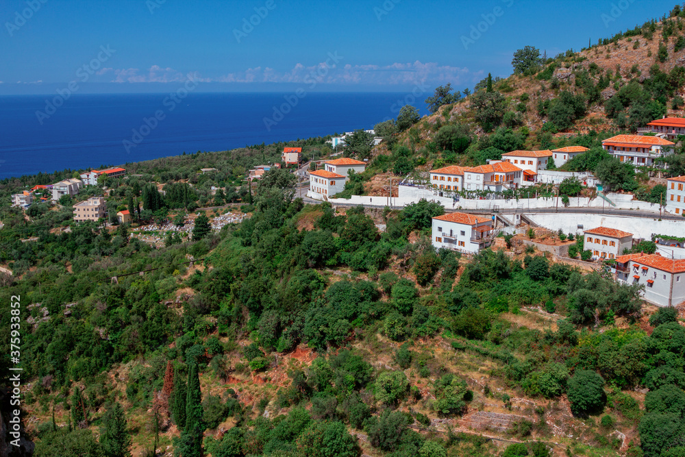 View of the village in Albania - traditional white houses with orange roofs and wooden shutters on windows - on the mountain hill, blue sky and sea on the horizon