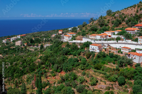 View of the village in Albania - traditional white houses with orange roofs and wooden shutters on windows - on the mountain hill, blue sky and sea on the horizon