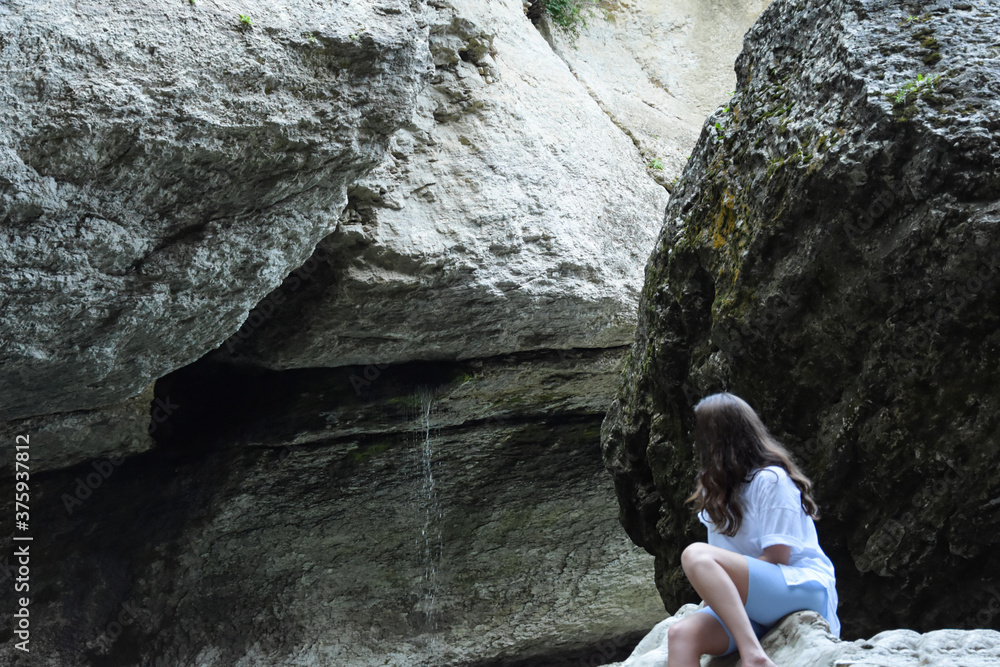 A young girl sits on a rock and watches the water flow down the rock. Gray rocks are everywhere, man is among the rocks. A young girl sits on a rock and watches the water flow down the rock. Gray rocks are everywhere, man is among the rocks.