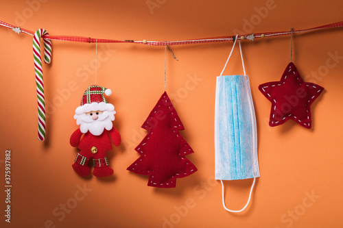 Christmas decorations and a medical mask hang on a decorative ribbon on a colored background. Quarantine concept for the new year © Sergey Chayko