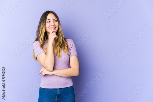 Young caucasian woman isolated on purple background relaxed thinking about something looking at a copy space.