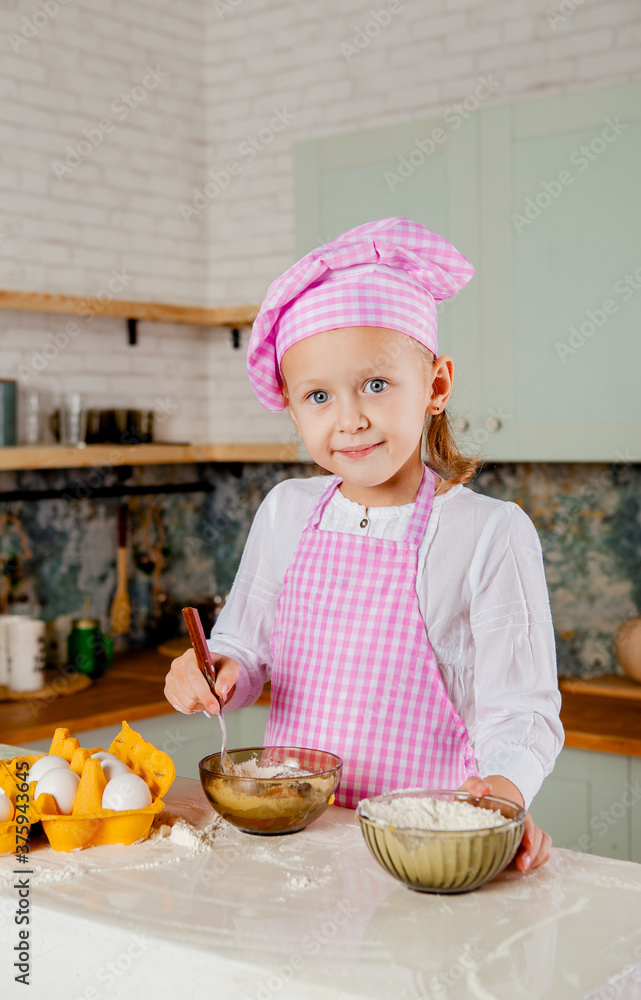 Girl in a chef's hat and apron kneads dough in the kitchen Girl in a chef's hat and apron kneads dough in the kitchen
