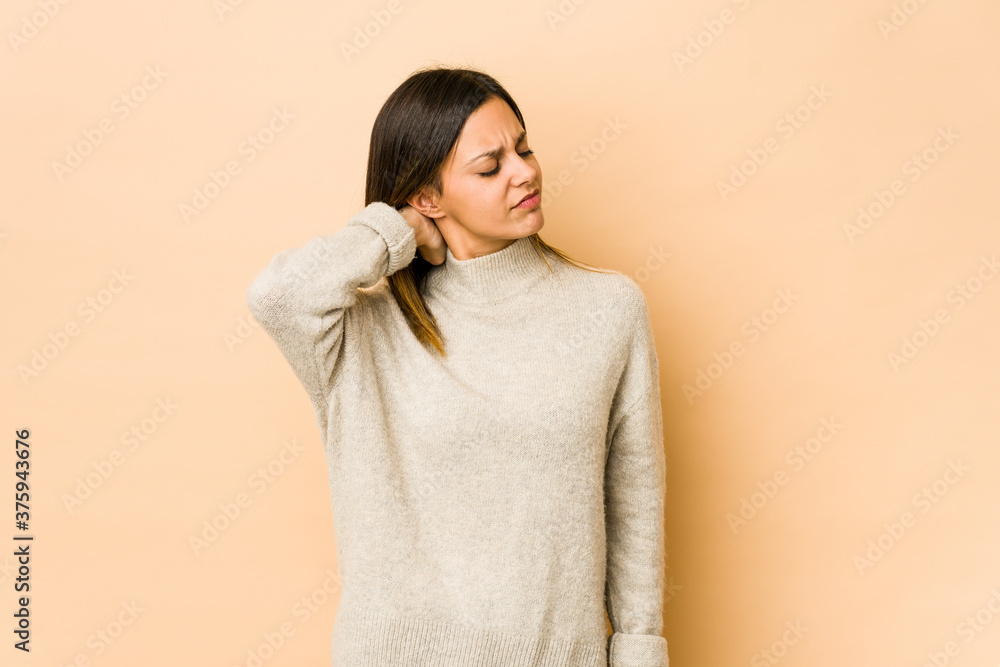 Young woman isolated on beige background having a neck pain due to stress, massaging and touching it with hand. Young woman isolated on beige background having a neck pain due to stress, massaging and touching it with hand.