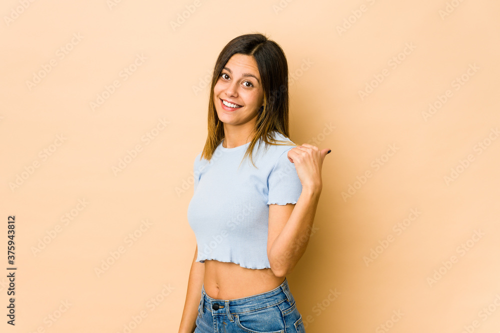 Young woman isolated on beige background points with thumb finger away, laughing and carefree. Young woman isolated on beige background points with thumb finger away, laughing and carefree.